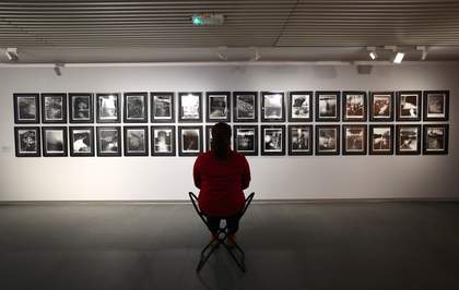 A photograph of a visitor sitting on a portable stool in front of some photographs