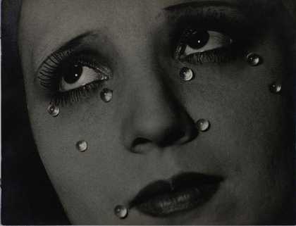 A black and white photographic portrait of a close up of a woman's face with glass tear drops at various places on her face